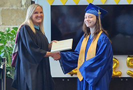  A woman and a girl in a graduation cap and gown hold a diploma